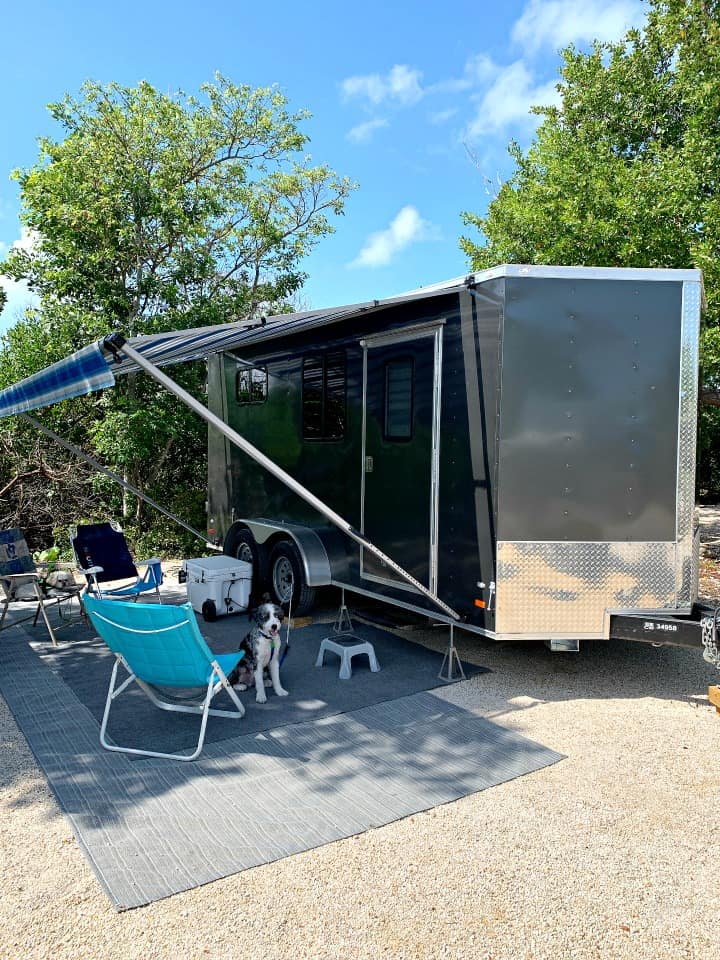 dark gray cargo trailer with blue awning parked on campsite at the beach