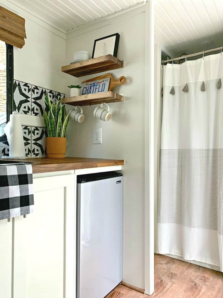 RV kitchen corner with wood shelves for storage that hold dishes and a picture
